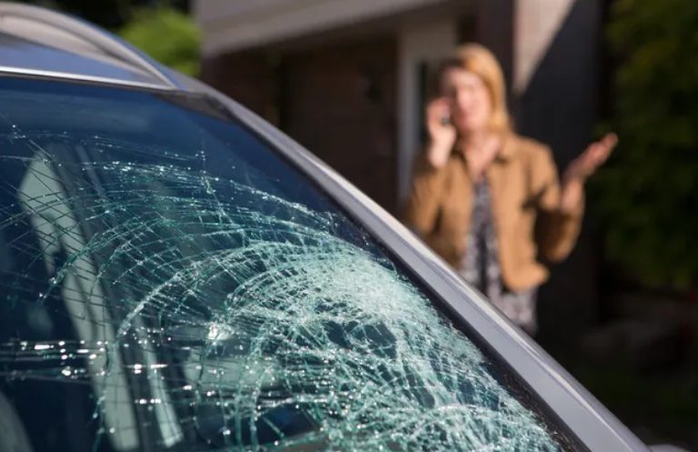 Broken Glass of the Broken Windshield After a Heavy Car Accident and at the Back Lady Talk Over Phone